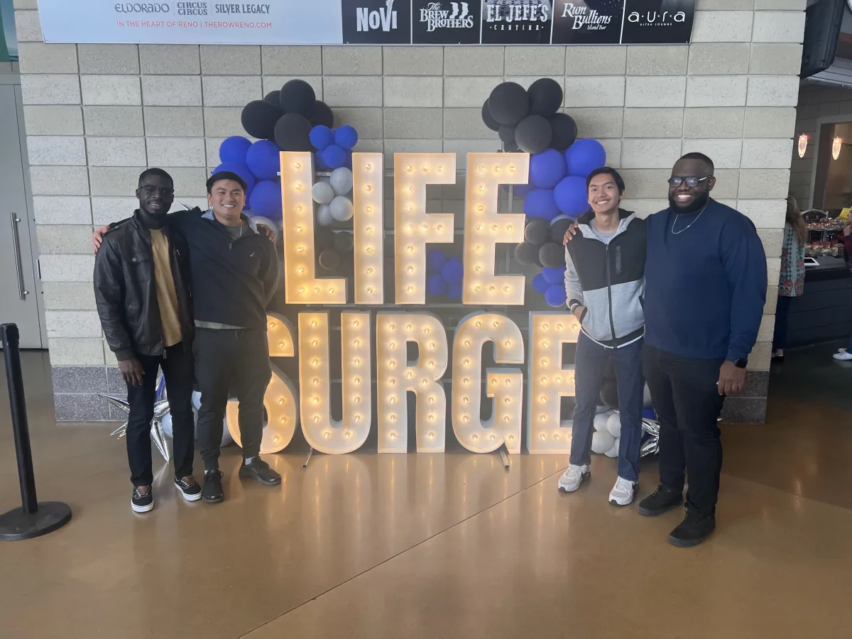 Anton and three friends beside a lit Life Surge sign.
